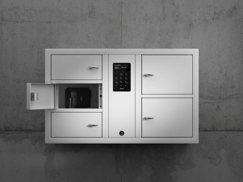 Valuables cabinet 7005 S in the System series. Mounted on the wall with open compartments containing a bag with personal belongings.